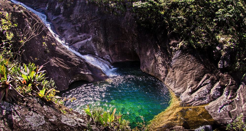 Poço verde-esmeralda entre paredes de rocha, com uma queda d'água