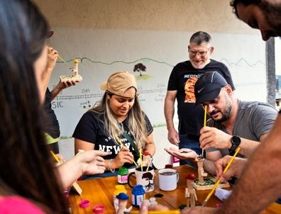 Participantes pintando peças de madeira numa oficina com artesão local