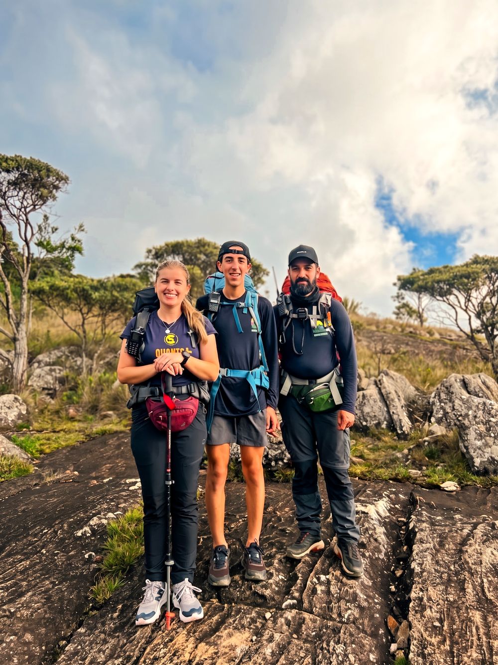 Kely, Pedro e Sairo, de mochila e rádio, numa laje de pedra no alto da serra