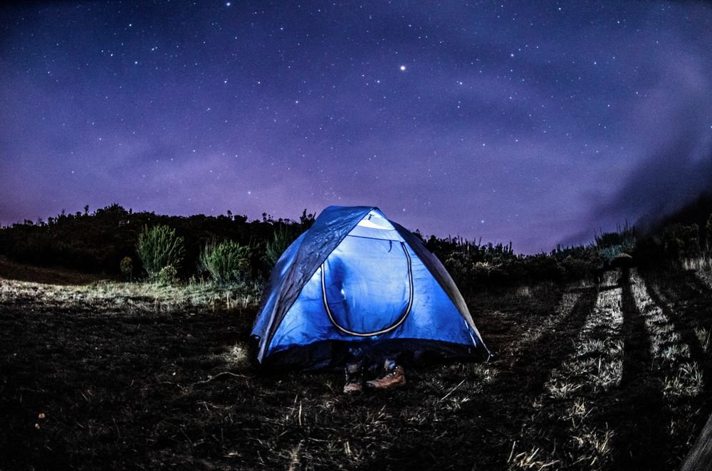 Barraca azul iluminada por dentro, sob o céu estrelado da serra