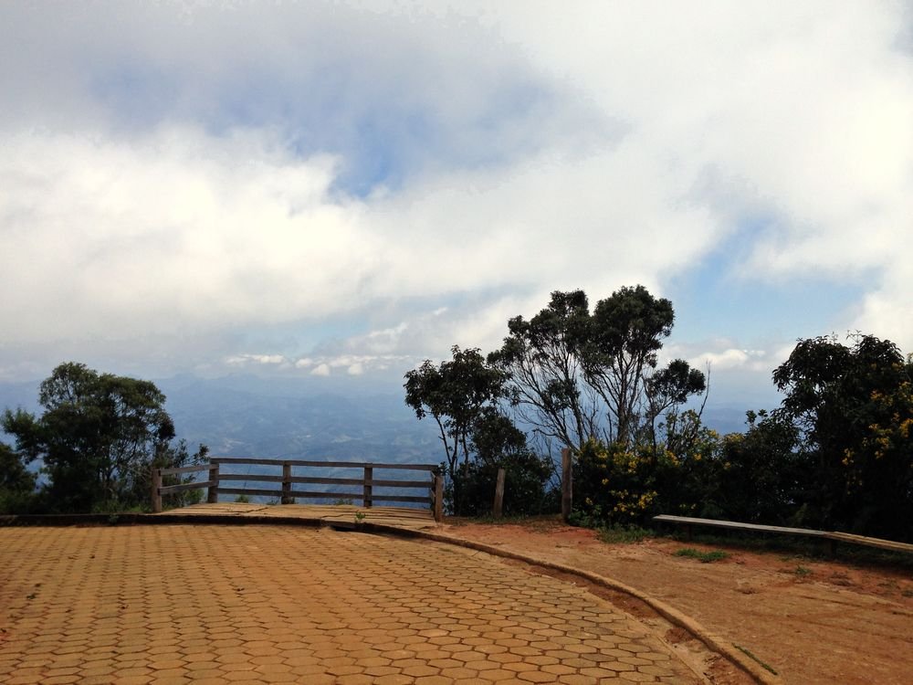 Mirante com piso de pedra e guarda-corpo de madeira, árvores e a serra coberta de nuvens