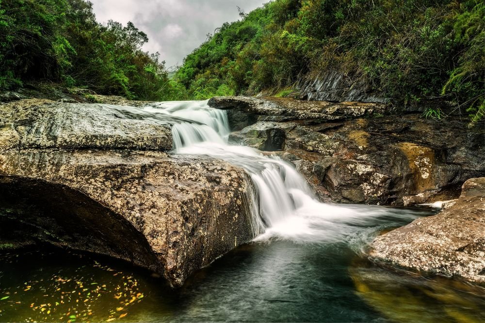 Cachoeira em degraus de pedra caindo num poço, entre a mata